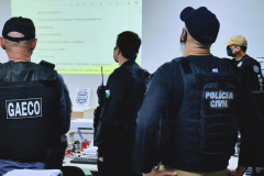 Policiais de costas observam apresentação de slides com dados da operação 