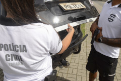 POlicial civil fecha tampa do porta-malas de viatura enquanto outro empunha arma