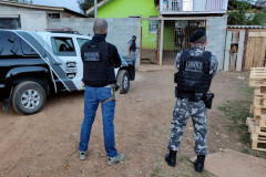 Policiais de costas, ao lado de viatura da polícia civil