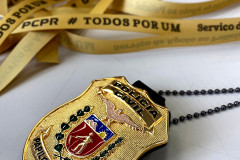 Escudo da policia civil em primeiro plano. ao fundo, fitas da campanha