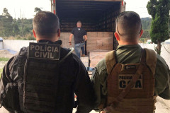 Dois policiais civis de costas observam caminhao recuperado