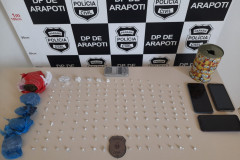 Droga apreendida sobre uma mesa. Ao fundo, banner da polícia civil.
