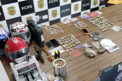 Material apreendido, sobre uma mesa. Ao fundo, banner da PCPR