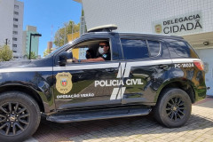 Policiais civis no interior de viatura em frente à delegacia cidadã