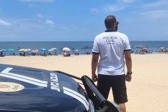 Policial civil ao lado de viatura observa veranistas