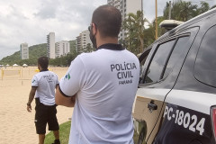 Dois policiais civis ao lado de viatura observam veranistas