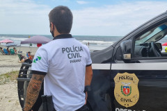 Policial civil ao lado de viatura observa veranistas