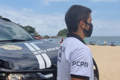 Policial civil ao lado de viatura observa veranistas