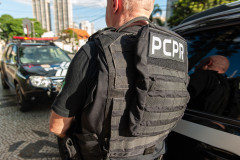 Policial civil de costas ao lado de viaturas