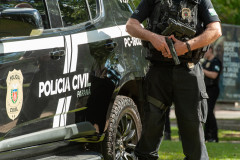 Policial civil empunha arma ao lado de viatura 