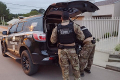 Dois policiais civis ao lado de viatura