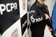 Policial civil empunhando arma ao lado de banner da PCPR