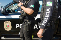 Dois policiais civis ao lado de viatura