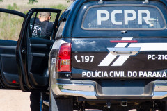 Policial civil ao lado de viatura apontando arma para suspeito