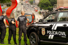 Três policiais civis ao lado de viatura