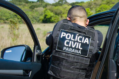 Policial civil apontando arma ao lado de viatura