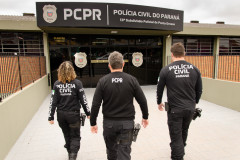 Três policiais civis de costas entrando em delegacia