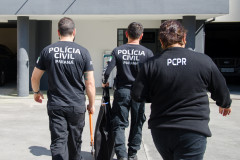 Três policiais civis de costas entrando em delegacia