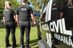 Dois policiais civis ao lado de viatura
