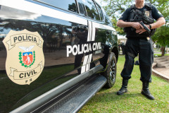 Policial civil empunhando arma ao lado de viatura