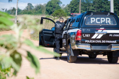 Policial civil apontando arma ao lado de viatura