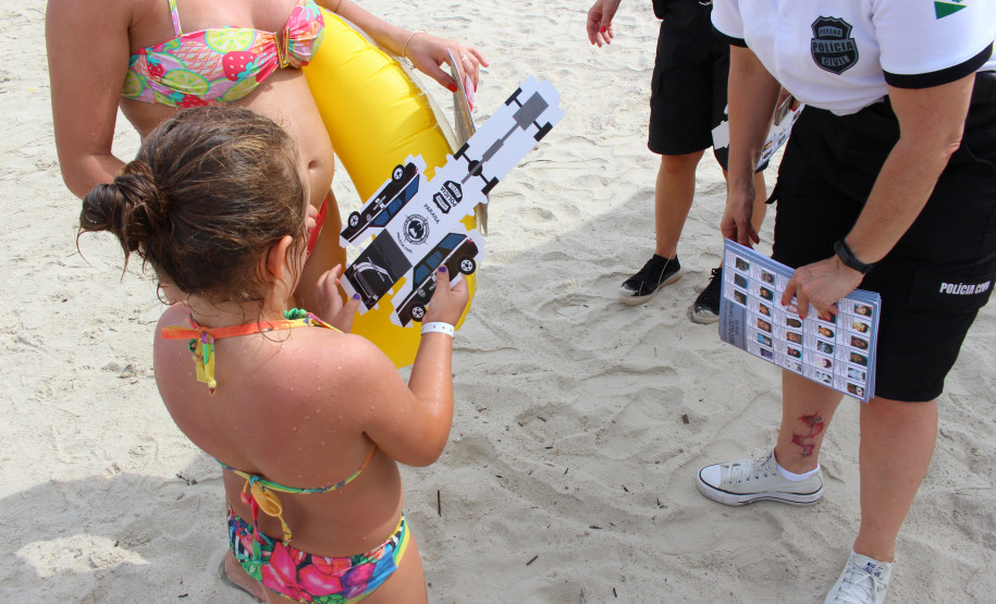 Policial civil distribuindo material preventivo na areia da praia para população