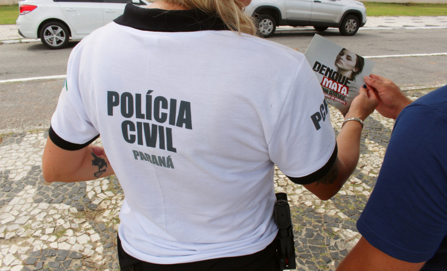 Polcial civil de costas entregando panfleto da campanha contra a dengue para um homem