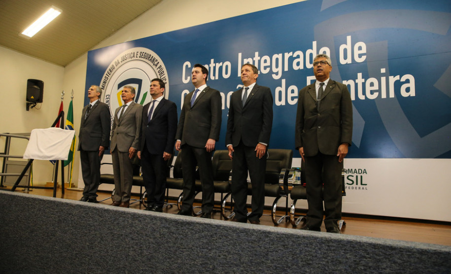 Autoridades no palco cantando o Hino Nacional