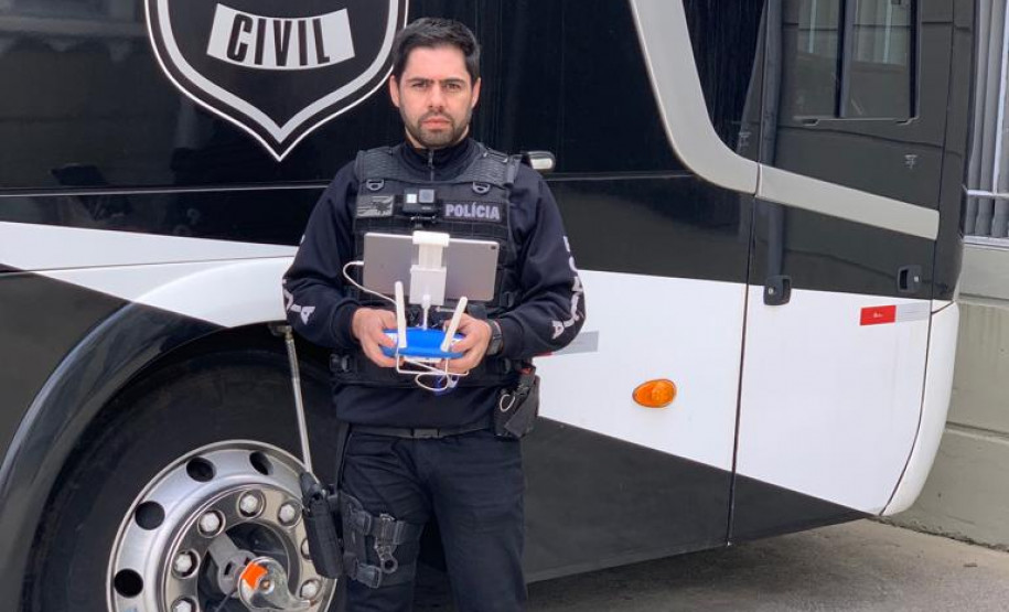 Investigador Juliano Filardo posa com drone e uniforme policial em frente a ônibus da PCPR