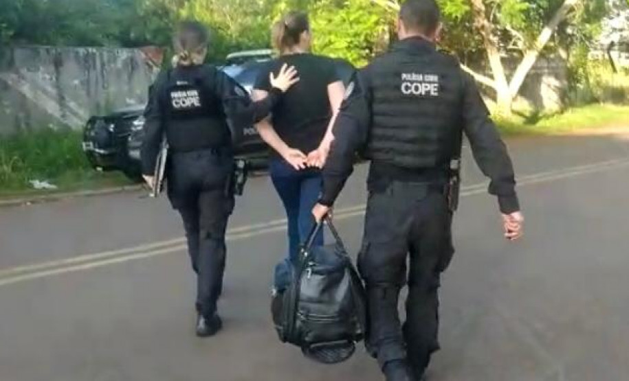 Dois policiais civis encaminhando um dos presos até a viatura