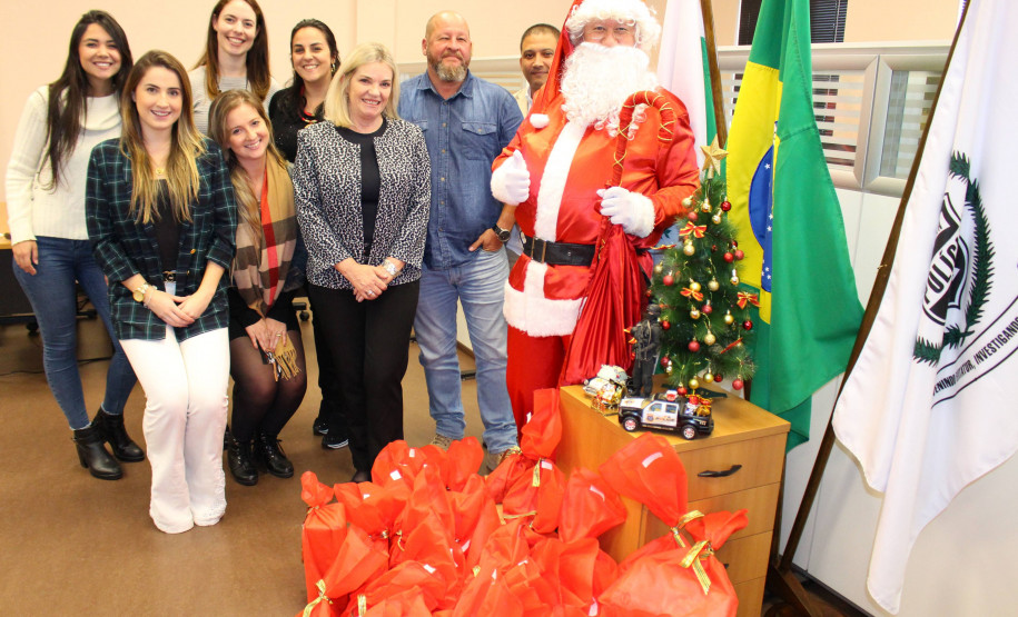 Policiais civis, presentes e papai noel em pé ao lado de um árvore de Natal