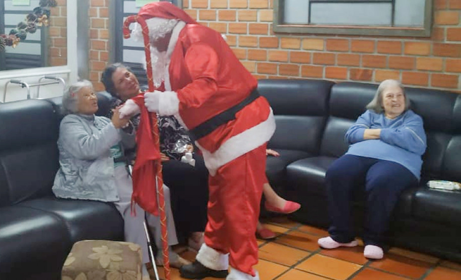 Papai Noel cumprimentando idosas no sofá do lar
