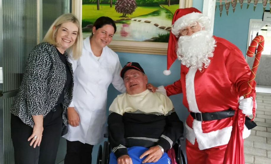 Delegada da PCPR, funcionária do lar de idosos, senhor cadeirante e papai Noel sorrindo para a foto