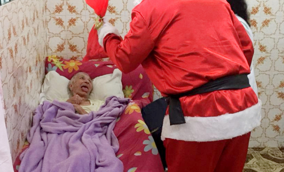 Papai Noel entregando presente para idosa acamada