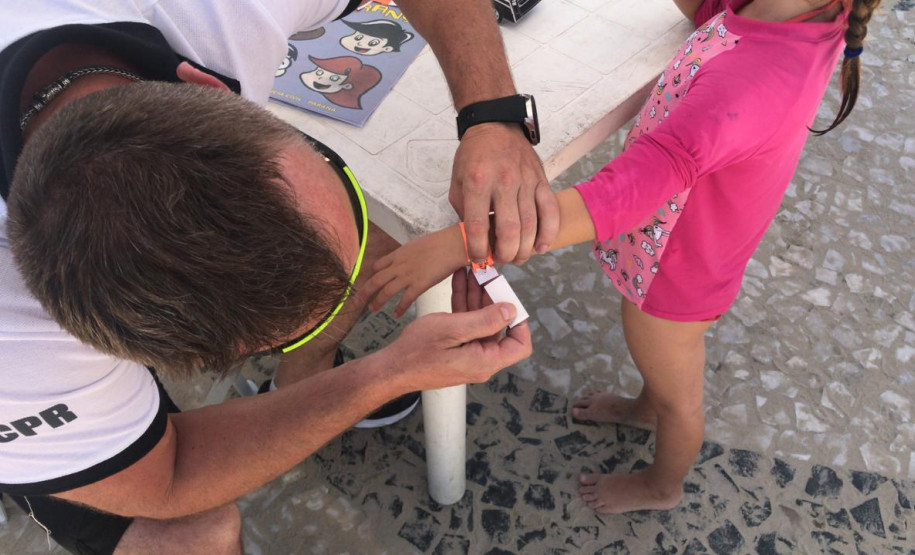 Policial da PCPR colocando pulseira de identificação em criança