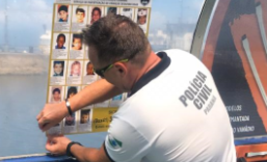 Policial da PCPR colando cartaz de crianças desaparecidas