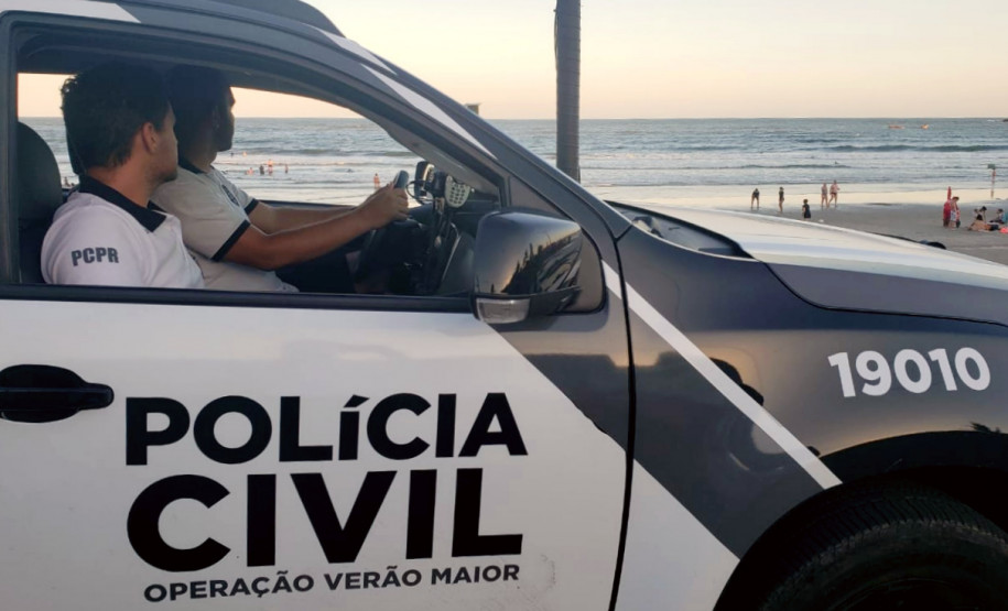 Dois policiais civis no interior de uma viatura, no litoral.