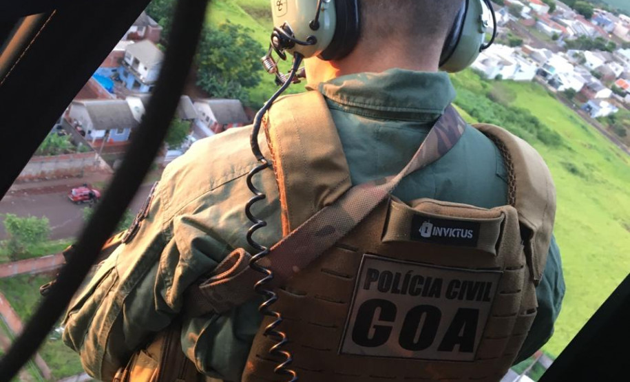 Policial civil dando apoio a bordo de helicóptero para equipes que atuam no solo