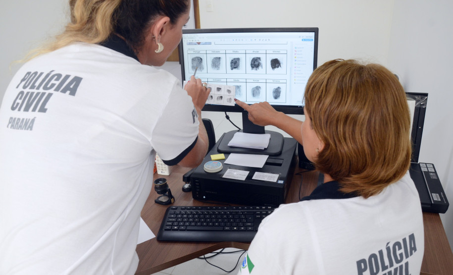 Duas policiais civis ao computador, trabalhando no sistema de identificação
