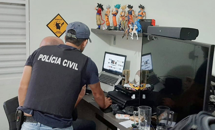 Policiais civis analisam notebook no interior de um quarto