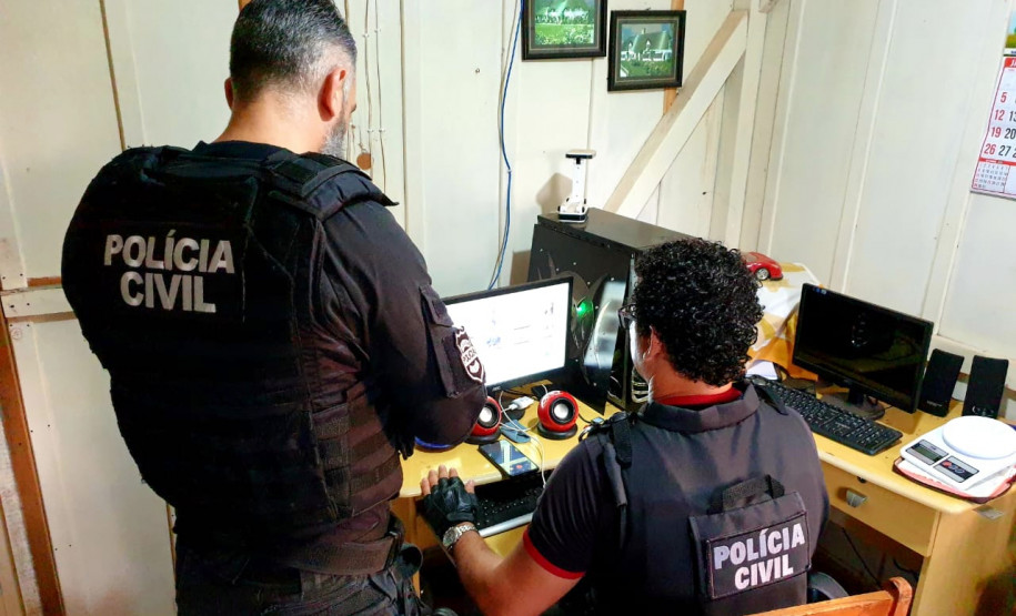 Policiais civis analisam computador no interior de um quarto