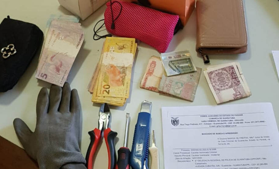 Carteiras, dinheiro, luva, alicate, estilete e chave de fenda sobre uma mesa