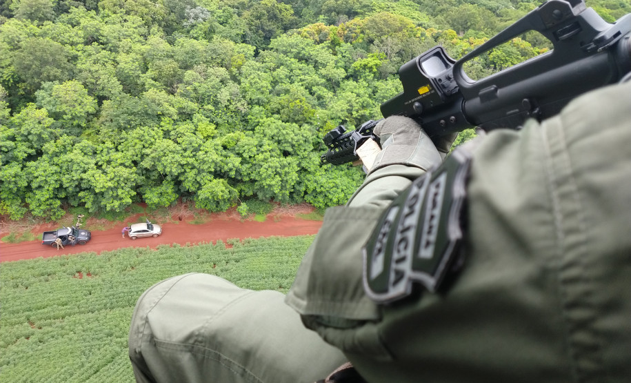 Policial civil em helicóptero apontando fuzil para abordagem terrestre