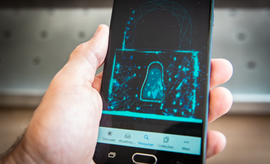 Mão segurando um celular , em primeiro plano, com uma ilustração de cadeado