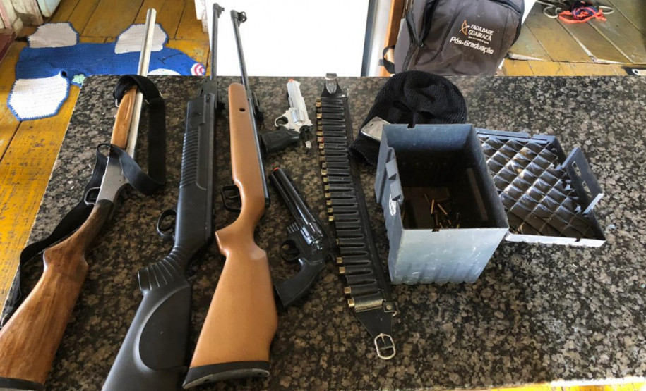 Sobre uma mesa, armas e munição apreendidas