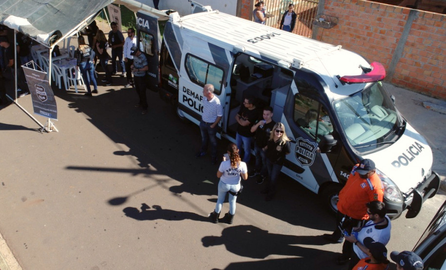 Imagem aérea mostrando policiais civis e demais pessoas junto ao veículo da PCPR
