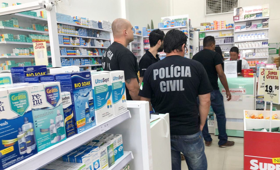 Policiais civis de costas, no interior de uma farmácia