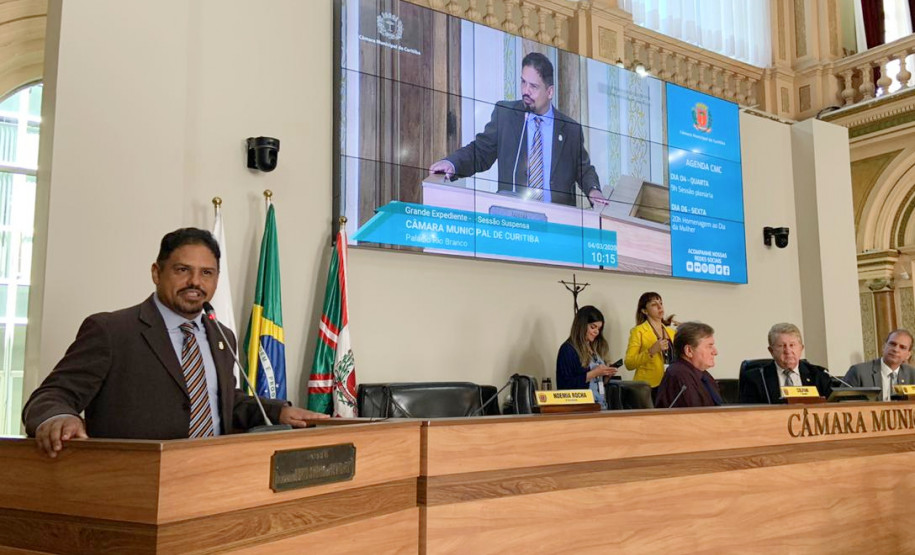 Homenageado discursando co m telão em segundo plano