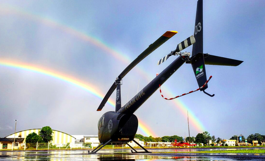Helicóptero da polícia civil em primeiro plano. Ao fundo, dois arco-íris