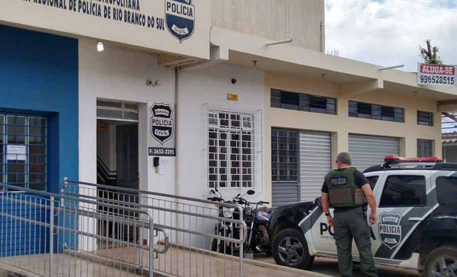 Fachada da Policia Civil de Rio Branco, com policial em pé, de costas, e viatura ao lado